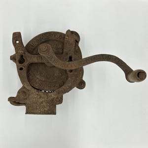 May include: An antique, cast iron hand-cranked grinder with a weathered, rusty finish. The grinder features a circular design with the text "U.S.A. MADE" and "BLACK HAWK" embossed on its surface. A wooden handle is attached to the crank.