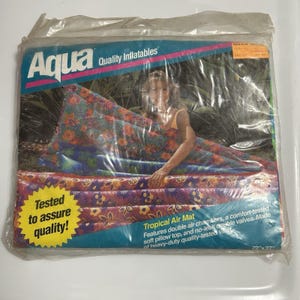 May include: An Aqua Quality Inflatables Tropical Air Mat in its original plastic packaging. The mat features a floral pattern in orange, purple, and blue. The packaging includes the text Tested to assure quality and measures 72 inches by 27 inches.