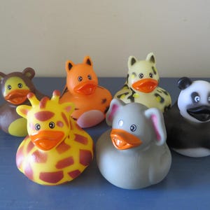 May include: A collection of six animal-themed rubber ducks. The ducks are designed to resemble a giraffe, bear, tiger, panda, elephant, and leopard. Each duck has an orange beak and is brightly colored.