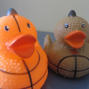 May include: Two rubber duck bath toys, one orange and one brown, both with a basketball design.