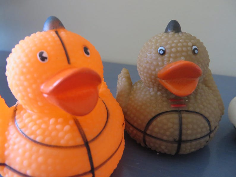 May include: Two rubber duck bath toys, one orange and one brown, both with a basketball design.