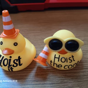 Op de afbeelding: Twee gele rubberen eendjes. E&eacute;n eend draagt een oranje en witte verkeerskegelhoed en heeft de tekst "Hoist it" op zijn lichaam. De andere eend draagt een gele zonnebril en heeft de tekst "Hoist the cone" op zijn lichaam.