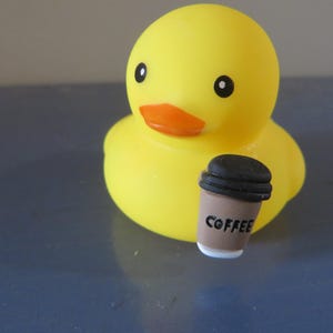 May include: A yellow rubber duck holding a brown coffee cup with the word "COFFEE" printed on it.