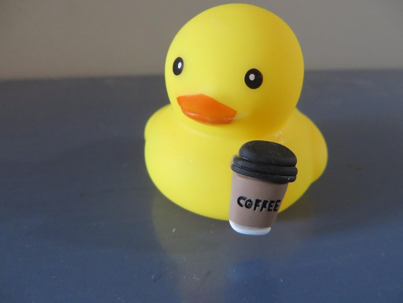 May include: A yellow rubber duck holding a brown coffee cup with the word "COFFEE" printed on it.