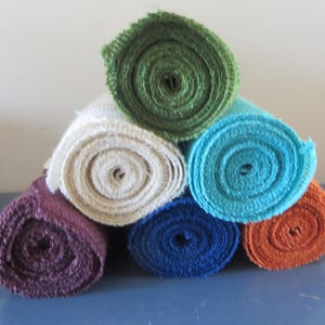 May include: Six rolls of burlap ribbon in various colors, including green, white, blue, brown, and orange. The rolls are stacked in a pyramid shape.