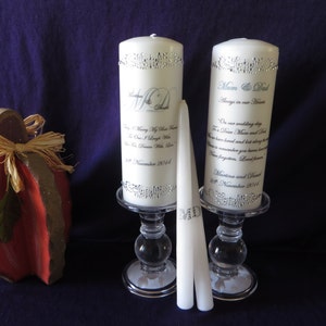 May include: Two white pillar candles with personalised messages and silver trim on glass candle holders. The candles are on a purple surface with a red wooden pumpkin ornament.