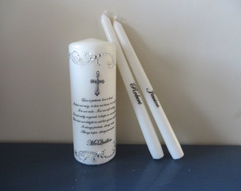 May include: Two white wedding unity candles with the names "Jessica" and "Robert" written on them. The larger candle has a silver cross and a quote about love printed on it. The quote ends with "McQuillen".