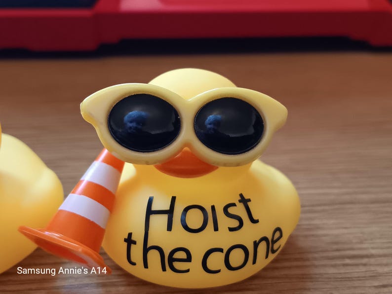 Op de afbeelding: Een gele rubberen eend met een zonnebril en een miniatuur oranje en witte verkeerskegel. De tekst "Hoist the cone" staat op het lichaam van de eend. Een leuk, nieuwigheid artikel.