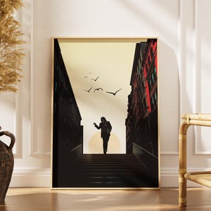 May include: A framed art print depicting a silhouetted figure descending a staircase between two buildings. The artwork has a warm colour palette with a yellow sky and red accents on the buildings. Birds are flying in the sky.