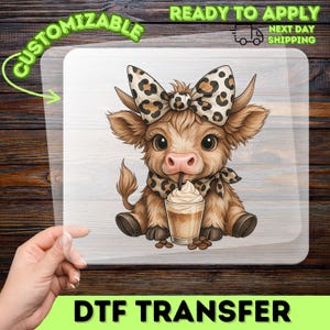 May include: A DTF transfer featuring a cartoon calf with a leopard print bow, scarf, and a drink with whipped cream. The calf is brown with large eyes and a pink nose. The transfer is on a clear background with the words "CUSTOMIZABLE" and "DTF TRANSFER".