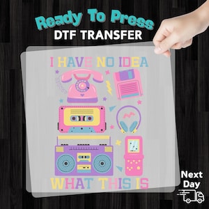 May include: A DTF transfer sheet featuring retro-themed graphics. The design includes a rotary phone, floppy disk, cassette tape, headphones, boombox, and handheld game console. Text reads "I HAVE NO IDEA WHAT THIS IS."