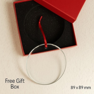 Pode incluir: Um enfeite circular de vidro transparente com uma fita vermelha, apresentado numa caixa de presente vermelha com interior preto. O texto "Free Gift Box" &eacute; vis&iacute;vel. O enfeite mede 8,9 x 8,9 cm.