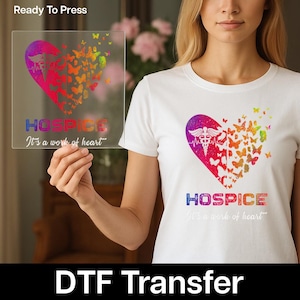 May include: White t-shirt with a heart-shaped design featuring a medical symbol, butterflies, and the word "HOSPICE." The design is in vibrant colors. The text "It's a work of heart" is below the word "HOSPICE."