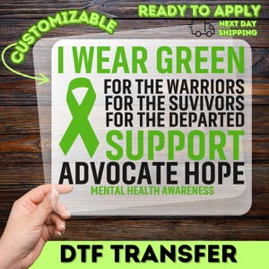 May include: A clear DTF transfer with the text "I WEAR GREEN" and a green ribbon, advocating for mental health awareness. The design includes the phrases "SUPPORT", "ADVOCATE HOPE", and "MENTAL HEALTH AWARENESS". The transfer is customizable and ready to apply.