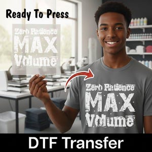 May include: A DTF transfer sheet featuring the white text Zero Patience MAX Volume in a distressed font style. The same graphic is applied to a grey t-shirt. A red arrow points from the transfer sheet to the graphic on the grey t-shirt.
