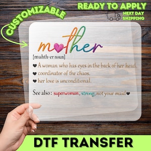 May include: A DTF transfer with the word "mother" in colorful embroidery-style lettering, a pink heart, and a definition. The definition includes phrases like "coordinator of the chaos" and "unconditional love." The transfer is labeled "Customizable."
