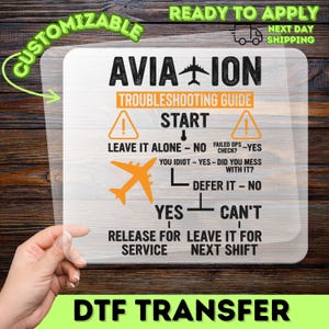 May include: Aviation troubleshooting guide DTF transfer with text. The design features the word "AVIATION" with an airplane graphic, a flowchart, and the words "CUSTOMIZABLE" and "READY TO APPLY". The transfer is held by a hand.
