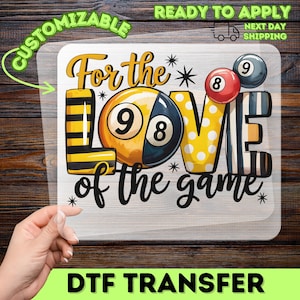 May include: A DTF transfer featuring the phrase "For the love of the game" with a billiards theme. The design includes a split 8-ball, a red 8-ball, a gray 9-ball, and the word "LOVE" in yellow with white polka dots. The word "LOVE" is between the 8-ball and the 9-ball.