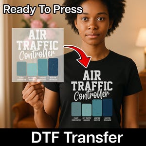 May include: A black t-shirt with the words "AIR TRAFFIC Controller" in white. Below the text are four blue-green rectangles with job titles. A clear DTF transfer with the same design is held up. The words "Ready To Press" and "DTF Transfer" are also visible.