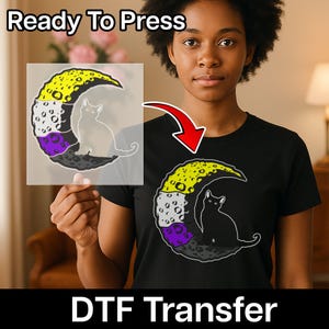 May include: Black t-shirt featuring a graphic of a cat inside a crescent moon with yellow, purple, and gray sections. The words "Ready To Press" and "DTF Transfer" are displayed in white text.