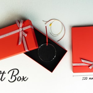 Pode incluir: Caixas de presente vermelhas com fita e la&ccedil;os prateados. Uma caixa est&aacute; aberta, revelando um interior preto e um adorno circular transparente. A caixa fechada mede 12 cm x 20 cm. O texto "Gift Box" est&aacute; escrito.