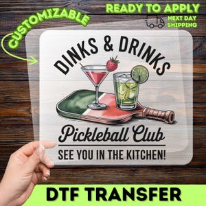 May include: A DTF transfer featuring a pickleball paddle with a cocktail and a drink. The text reads "Dinks & Drinks" and "Pickleball Club SEE YOU IN THE KITCHEN!" with the words "CUSTOMIZABLE" and "READY TO APPLY" at the top.