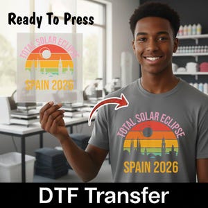 May include: A grey t-shirt featuring a graphic of a total solar eclipse over a city skyline with the text Total Solar Eclipse Spain 2026. The design includes a sunset-colored semi-circle and a dark eclipse circle against a light grey background.