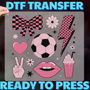 May include: DTF transfer sheet with various pink and black graphics, including a bow, soccer ball, lightning bolt, heart, peace sign, flowers, lips, and a milkshake. The text "DTF TRANSFER" and "READY TO PRESS" are displayed in blue.