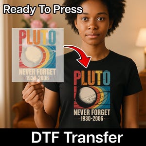 May include: Black t-shirt with a Pluto graphic in retro colors. The design includes the word "PLUTO", a planet illustration, and the text "NEVER FORGET 1930-2006". The image also shows a "Ready To Press" DTF transfer.