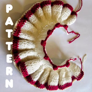 May include: A crescent-shaped crochet collar featuring a white base with deep red trim along the ruffled edges and small red bobble accents. The word PATTERN is printed vertically in white letters on the left side of the crochet piece.