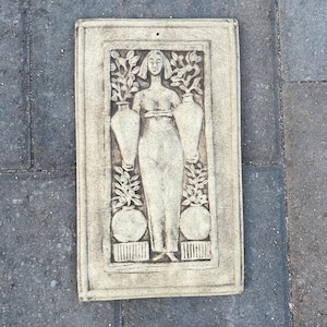 Puede incluir: Una placa de pared rectangular de piedra beige con un relieve de una figura central de pie entre dos jarrones grandes y dos macetas redondas más pequeñas, todo rodeado de ramas con hojas, con un pequeño orificio en el centro superior.
