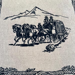 Op de afbeelding: Een lichtgrijs textiel met een donkerzwarte geweven illustratie van een postkoets getrokken door vier paarden, met twee figuren bovenop. De sc&egrave;ne bevat een bergketen op de achtergrond en een decoratieve rand van touw.