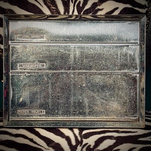 May include: A rectangular, brushed metal kitchen organizer with three compartments labeled "FOIL WRAP", "WAX PAPER", and "PAPER TOWELS". The organizer has a slightly distressed appearance and is set against a zebra-print background.