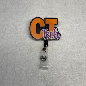 May include: A badge reel with the text "CT Tech" in orange and purple. The badge reel has a black cord and a clear plastic strap with a metal snap. The background is a light gray fabric.
