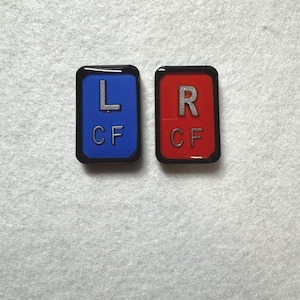 May include: Two rectangular, black-bordered patches. One is blue with a silver "L" and "CF", the other is red with a silver "R" and "CF".