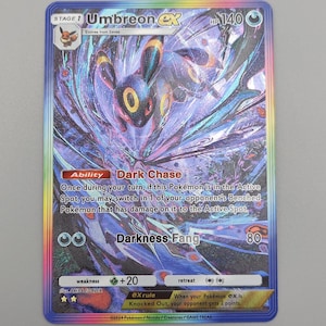 May include: Umbreon EX Pokémon trading card. The card features a holographic image of Umbreon with a dark and purple colour scheme. The card has text that includes the name, stage, and attack details.