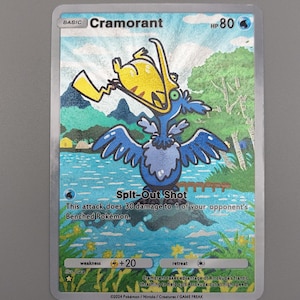 May include: A holographic Pokémon trading card featuring Cramorant. The card shows a blue bird-like creature with a yellow object in its beak, set against a landscape with water and trees. The text "Cramorant" and "Spit-Out Shot" are visible.