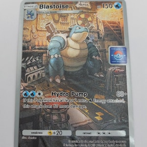 Peut inclure: Une carte à collectionner Pokémon Blastoise. La carte présente un personnage Blastoise bleu avec un arrière-plan détaillé. La carte contient le texte "Hydro Pump" et "HP 150". La carte est de la collection 2024 Pokémon/Nintendo/Creatures/GAME FREAK.
