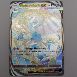 May include: A holographic Mega Altaria EX Pokémon card. The card features a large, cloud-like creature in shades of blue and white with gold accents. Text includes "Mega Harmony" and "190 HP".