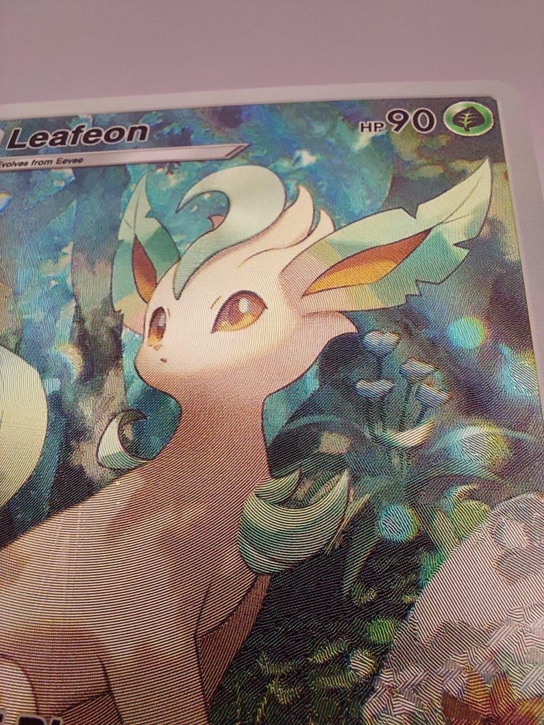May include: A holographic trading card featuring Leafeon, a green and tan Pok&eacute;mon. The card has a forest background and the HP is 90. The card is from the Eevee evolution line.