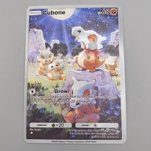 May include: A Cubone Pokémon trading card featuring a Cubone character with a bone helmet. The card has a colorful illustration of Cubone in a grassy landscape with the text "Growl" and "HP 60". The card also has the text "weakness +20" and "retreat".