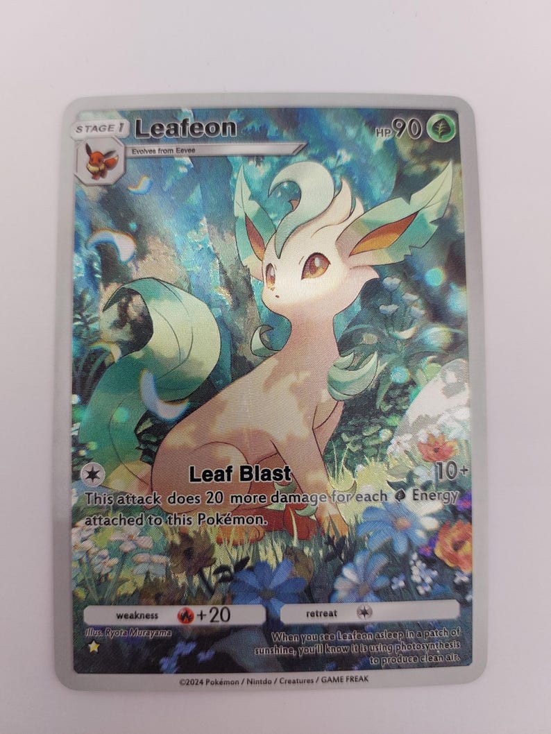 May include: A holographic Pok&eacute;mon trading card featuring Leafeon, a grass-type Pok&eacute;mon. The card has a colourful background with flowers and foliage. The text on the card includes "Leaf Blast" and "HP 90".