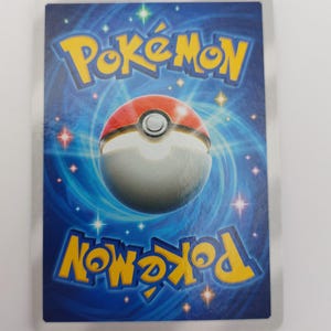 May include: Reverse side of a Pok&eacute;mon trading card. The card has a blue background with a swirling pattern and white stars. The Pok&eacute;mon logo is in yellow, with a red and white Pok&eacute; Ball design in the centre.