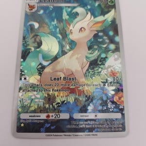 May include: A Pok&eacute;mon trading card featuring Leafeon, a green and tan creature, set against a floral background. The card includes text such as "Leaf Blast" and "+20". The card is from 2024.