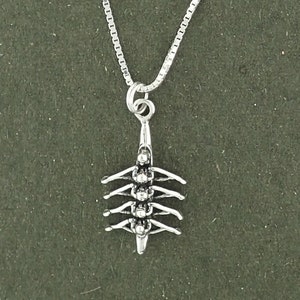 May include: Silver necklace with a charm of a rowing crew in a boat. The charm is detailed and shows the rowers in action.