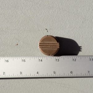 May include: A circular brown knob with a ribbed edge and three horizontal lines across the center. The knob is positioned above a metal ruler, showing a diameter of approximately 1.25 inches. The object has a matte finish and a flat top surface.