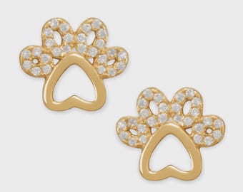 May include: A pair of gold-colored paw print stud earrings. Each earring features a paw print design with a heart-shaped center and is encrusted with small, clear gemstones. The earrings are set against a light gray background.