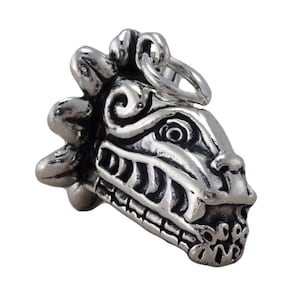 May include: A silver-toned metal pendant shaped like a stylized serpent head with intricate carved details, including a prominent crest, defined eye, and visible teeth. The piece features a polished finish with darkened recessed areas and a jump ring.