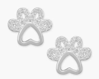 May include: A pair of silver-colored paw print stud earrings. Each earring features a paw print design with a heart-shaped center and small, round accents. The earrings are set against a white background.