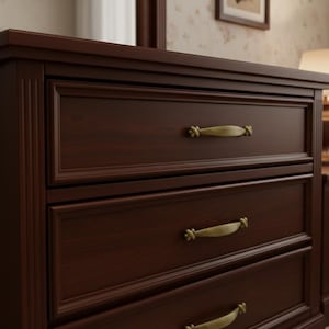 Könnte beinhalten: Eine dunkelbraune Holzkommode mit drei Schubladen. Jede Schublade hat einen goldfarbenen Griff. Die Kommode ist Teil eines Schlafzimmermöbelsets. Die Holzmaserung ist sichtbar.